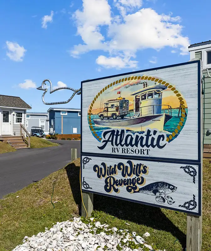 Painted wooden entrance sign for Atlantic RV Resort and Wild Will's Revenge with boat artwork, cabins and paved drive