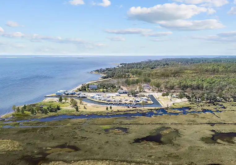 Aerial photo of a coastal marina and RV park on a peninsula, surrounded by marshland, pine forest and open bay water.